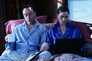 Couple in bed, doing their own thing.