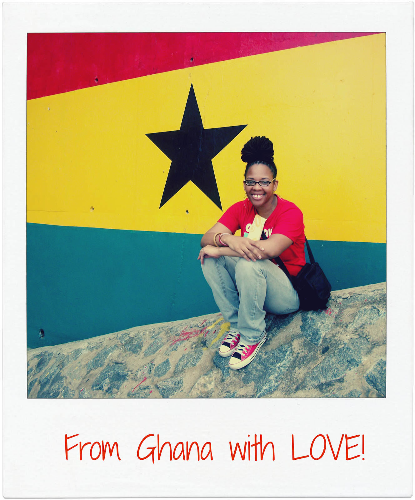 From Ghana With Love International Artist, Jolyn Gardner Campbell Smiles While Sitting in front of a Hand Painted Ghana Flag on a Concrete Wall.