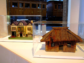 A vintage doll's house and model hut on display in a museum.
