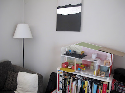 A bookcase in a lounge, with a half-built Lundby dolls' house on top of it.