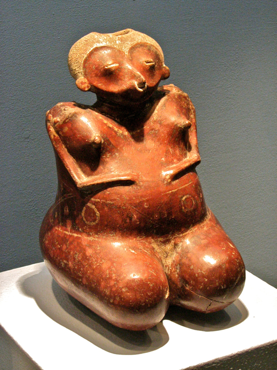 Pregnant figure is nude, except for tattoos, a necklace, and a nose ring. Pregnant figure is nude, except for tattoos, a necklace, and a nose ring.