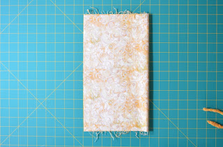 Fabric is laid out on cutting mat grid and is folded vertically with the fold on the right hand side and the two straight sides meeting at the left hand side.