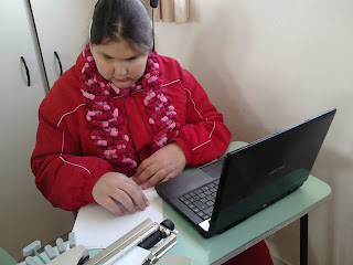 Foto da Kelli pesquisando na tabela em Braille para responder as questões da prova