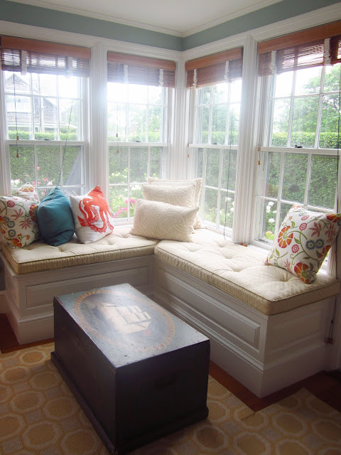 window bench with accent pillows, a wooden chest with a ship painted on it and a yellow rug