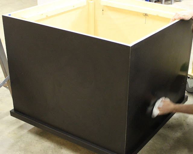 The casework gets spruced up for its opening A young man's hands can be seen holding a white rag and carefully wiping down the black laminate of the casework; preparing it to roll out on the floor.