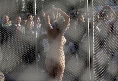 stands naked with her wrists chained to a gate