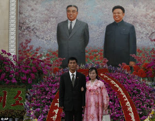 Couple poses in front of a mural of Kim Il Sung and Kim Jong Il