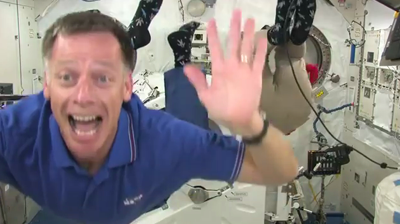 Atlantis – STS135 – Commander Chris Ferguson doing a flip-back during an interview with the media, joined by Dr Sandy Magnus in the background. NASA-TV 2011.