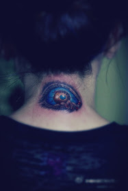A tattoo featuring a blue eye behind the neck.