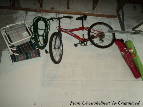 From Overwhelmed to Organized. Bicycle, lawn chairs and hoses hung on hooks in garage wall.