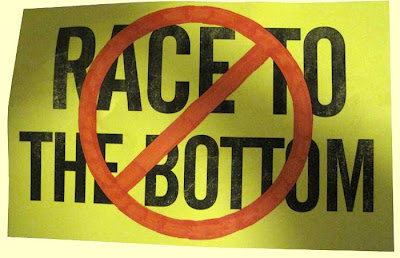 Fluorescent yellow sign reading RACE TO THE BOTTOM with a red circle and slash through it