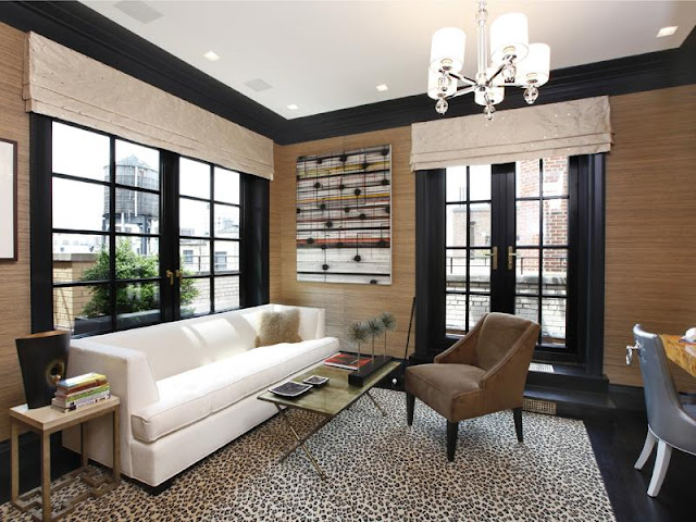 Living room in an apartment with black floors, a cheetah print rug, natural grass wallpaper, black french doors, black lacquer trim molding, a white sofa, a brown arm chair and a chandelier 