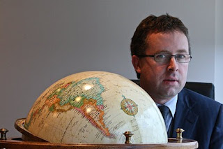 a man in a suit and tie behind a globe