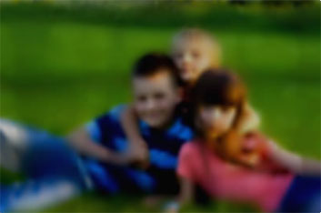 Blurry image of three kids posing for a photo laying on grass.