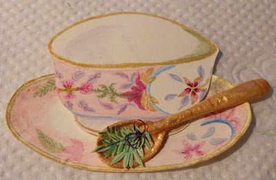 Handmade paper tea cup, really cute, over a matching plate with an embossed golden spoon with lavender twigs tied with a purple bow on it
