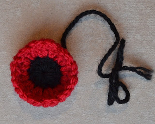A rounded 'mini poppy' with a black centre and cupped red stitches to represent petals. A black thread is still attached.