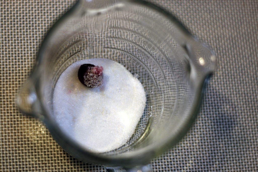 A cup with some granular sugar and a single cranberry rolled in the sugar.