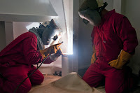 NNS welder Shaun Woroneski (left) welds a time capsule containing commemorative items into the island of the aircraft carrier Gerald R. Ford (CVN 78) while NNS fitter Jerry Womack looks on Time capsule