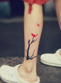 A tattoo featuring a red bird resting on a black tree and another bird flying away