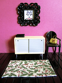Modern doll's house miniature hallway with black floorboards and berry-coloured wall. On the floor is a cream rug with a pattern of leaves and berry stalks in soft greens,  berry colours and black.