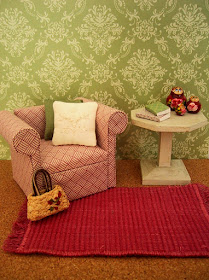 Modern dolls' house miniature pink and white armchair and white side table on a pink woven rug.