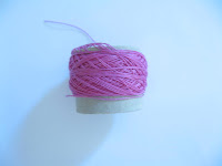 Side view of small cardboard reel of hot pink size 80 cotton thread.
