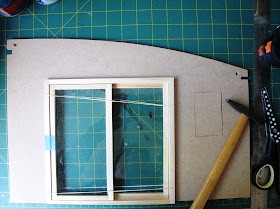 Side wall of a dolls house kit, with a hole cut for the sliding doors (which are in the hole) and a piece of wood inserted into a previously-cut window opening.