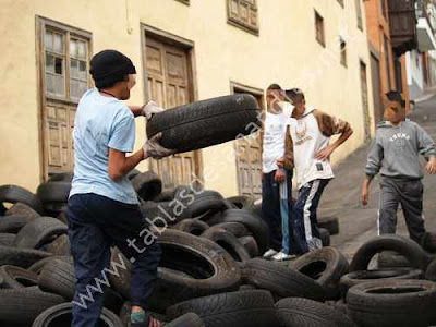 Unos muchachos acondicionan una pila de neumáticos en la Calle de San Antonio