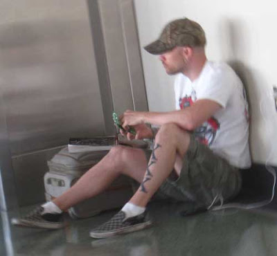 Young man sitting on floor wearing shorts, side of his leg appears to have KKK tattooed along his shin