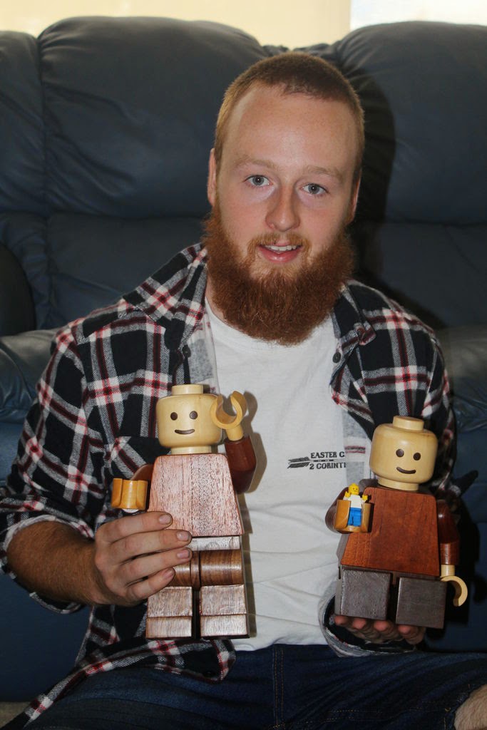 man with beard holding two wooden lego men, one which is holding small plastic lego man