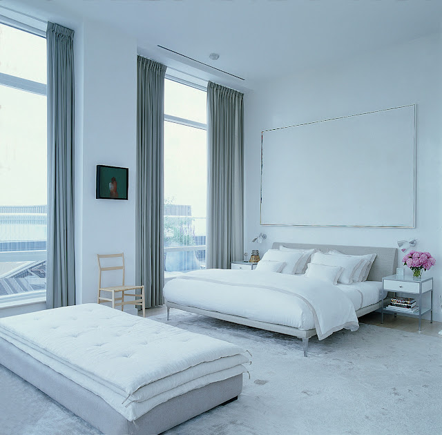 modern grey and white bedroom with upholstered headboard, large windows with floor length curtains and a long ottoman