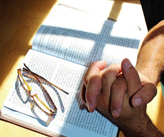 Hands folded in prayer resting on an open Bible
