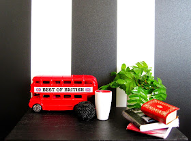 Modern miniature black table displaying a model London bus, vases, books and a plant in black, white and red.