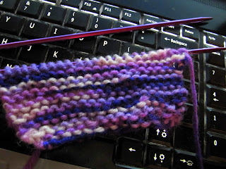 small rectangle of knit and pearl stitches in purple variegated yarn laying on a laptop keyboard.