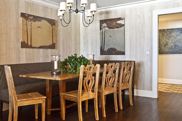 Dining room with grey stained wood walls, a wire chandelier, four carved wood chairs, a farmhouse style wood table and black and gold poka dot banquette seating 