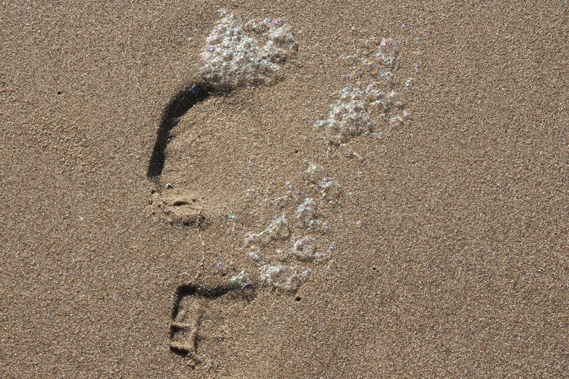 footstep in sand with sea foam footstep in sand with sea foam
