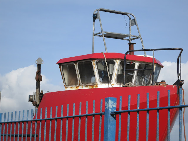 Old red fishing boat behind bright blue railings.