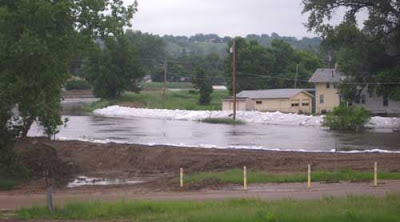 Flooded narrow river with dirt and white plastic levees built along it