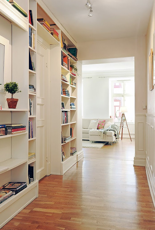 Foyer in a Swedish apartment with built in bookshelves, wood floor and a view of the living room