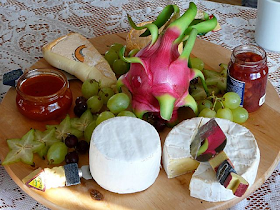 Luxurious cheese platter, with brie, grapes, pickle and more - decorated with flowers and on a wooden cheeseboard.