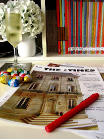 Printed out proofs of The tiny Times magazine on a desk, along with red pen, glass of sparkling wine and pile of small easter eggs.