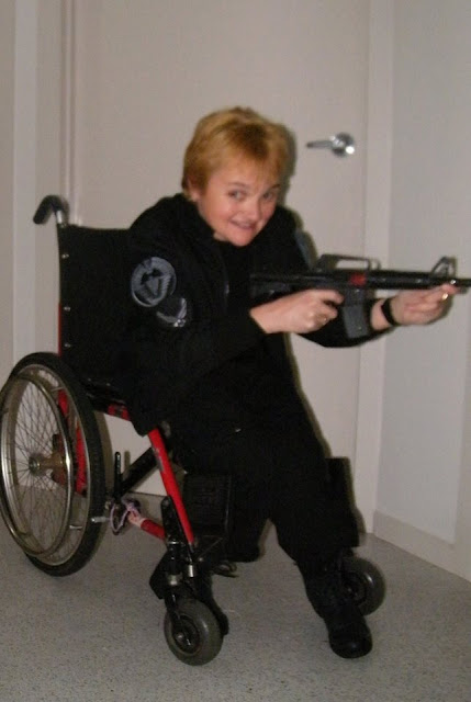 Kellie, in a wheelchair, dressed up in a costume, holding a gun