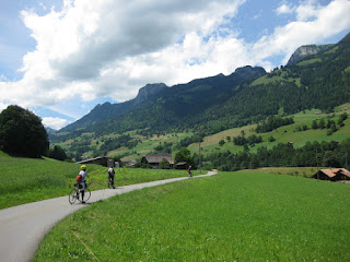 Cyclists along a rural road, with blue skies and puffy clouds over the hills, en route to Lenk im Simmental, Switzerland