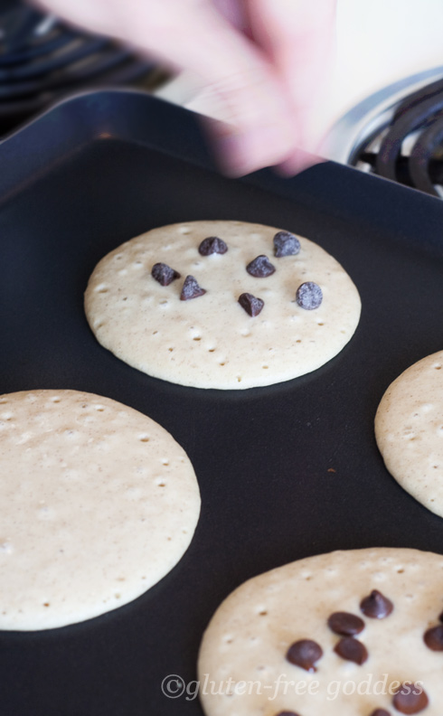 Gluten-free pancakes on the griddle- adding chocolate chips. Gluten-free pancakes on the griddle.