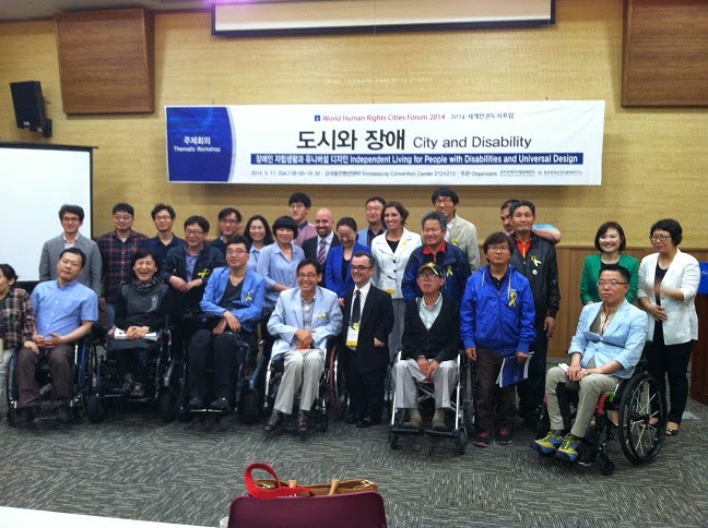image of group of about thirty people, some in wheelchairs, posing in front of room for photo