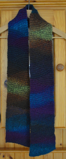 Shadow Spectrum slip stitch scarf on a coathanger hanging on a pine dresser.