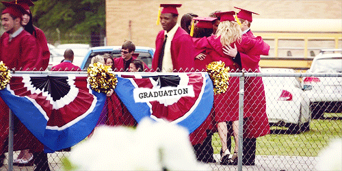 Gif of the characters from The Vampire Diaries hugging. They wear red graduation robes and stand behind a chain link fence with a red, white, and blue graduation banner draped over it.