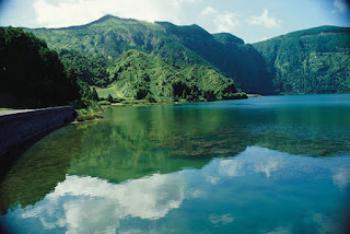 [acqua di lago dalle montagne dove c'è un paesaggio: bosco,cielo,sole]