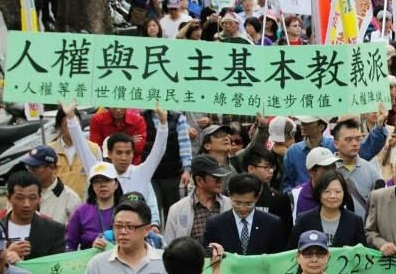 2014 年二二八大遊行陳立民 Chen Lih Ming (陳哲) 與「人權陣線」戰友高舉「人權與民主基本教義」大幅走在蔡英文主席之後，陳哲 CLM 為畫面中「主」字下仰頭者