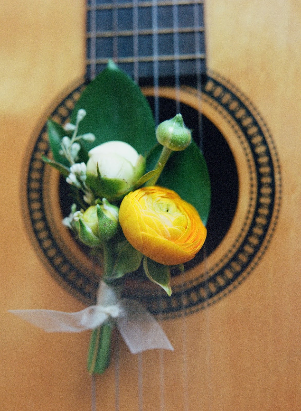 yellow ranunculus and peony spring boutonniere resting on an acoustic guitar